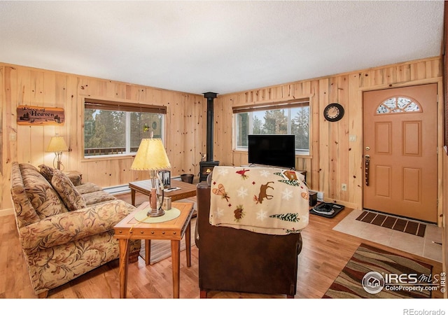 living area featuring a baseboard radiator, a wood stove, wooden walls, and wood finished floors