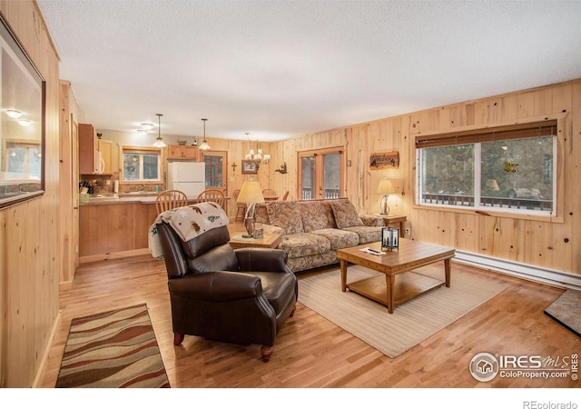 living area with light wood finished floors, a chandelier, baseboard heating, and a textured ceiling