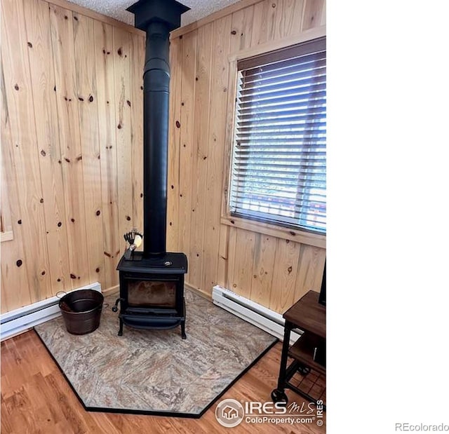 details featuring a baseboard heating unit, a wood stove, wooden walls, a textured ceiling, and wood finished floors