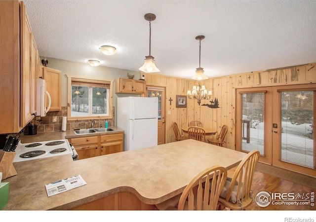 kitchen featuring white appliances, a peninsula, hanging light fixtures, light countertops, and a sink