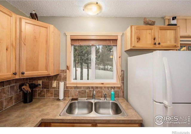 kitchen featuring light brown cabinetry, a sink, freestanding refrigerator, and decorative backsplash