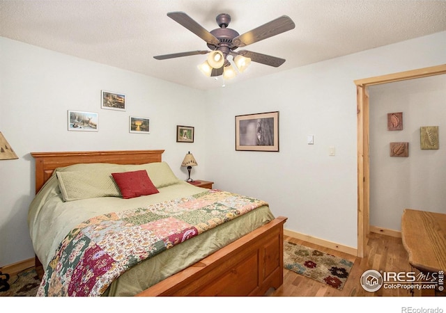 bedroom with light wood-style flooring, a textured ceiling, baseboards, and a ceiling fan