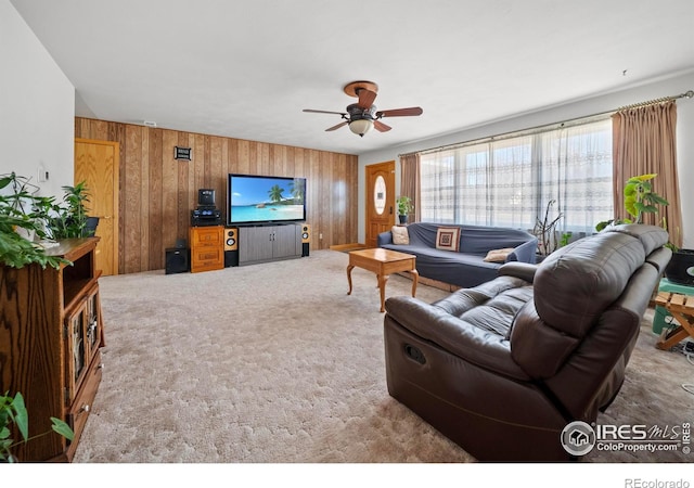 living area featuring wood walls, ceiling fan, and carpet flooring