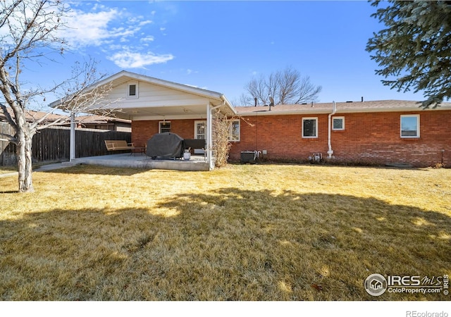 back of house featuring brick siding, a patio, a lawn, and fence