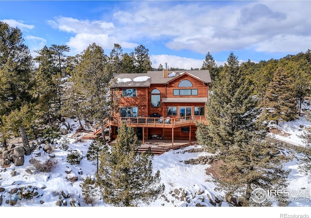 snow covered property with a deck, a chimney, and stairs