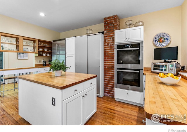 kitchen with double oven, butcher block countertops, wood finished floors, white cabinetry, and a center island