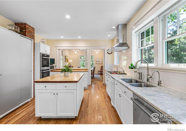 kitchen with stainless steel appliances, white cabinetry, a sink, wood counters, and wall chimney range hood