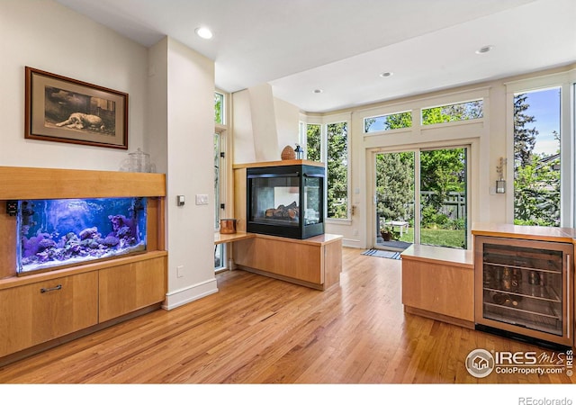 living room featuring beverage cooler, baseboards, light wood-type flooring, a multi sided fireplace, and recessed lighting