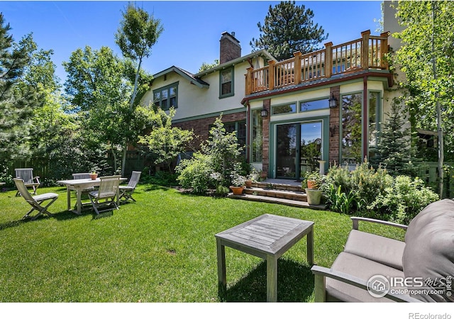 rear view of property featuring brick siding, a balcony, a chimney, a yard, and stucco siding