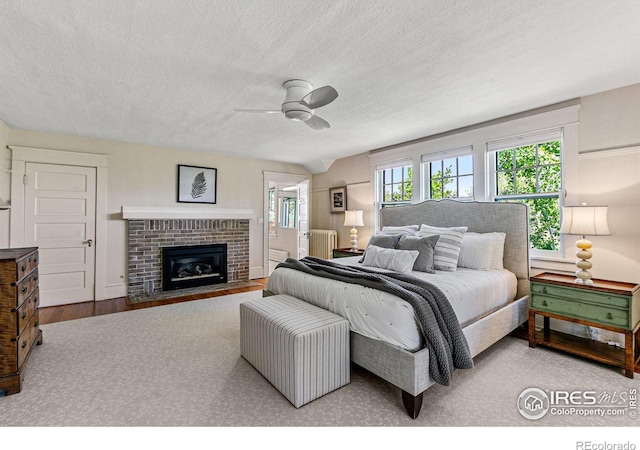 bedroom with radiator heating unit, ceiling fan, wood finished floors, a textured ceiling, and a brick fireplace