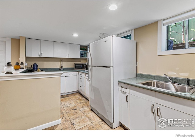 kitchen featuring stainless steel microwave, freestanding refrigerator, stone finish floor, white cabinetry, and a sink