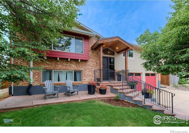 view of front of house with a garage, brick siding, a front yard, driveway, and a patio area