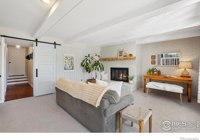 living area featuring carpet, a fireplace, beamed ceiling, and a barn door