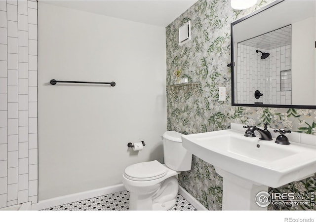 bathroom featuring wallpapered walls, baseboards, tiled shower, toilet, and tile patterned flooring