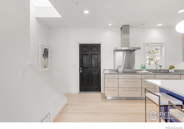 kitchen with light wood finished floors, wall chimney exhaust hood, recessed lighting, a sink, and baseboards