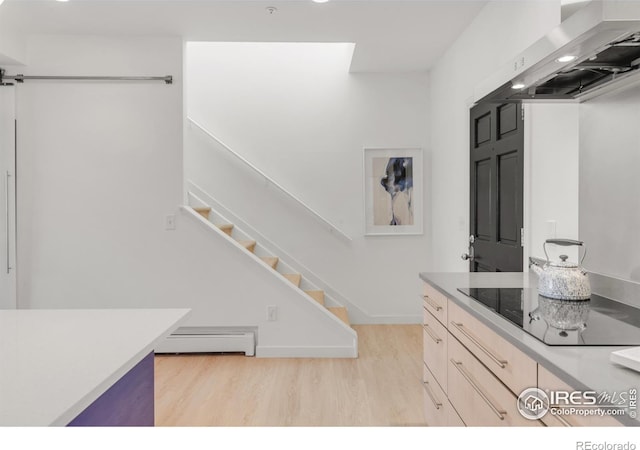 kitchen with wall chimney exhaust hood, black electric stovetop, baseboard heating, light countertops, and light wood-type flooring