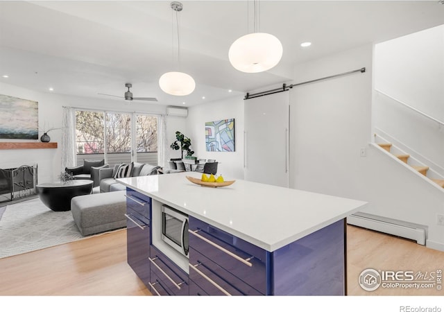 kitchen featuring a barn door, light wood-style floors, blue cabinetry, baseboard heating, and stainless steel microwave