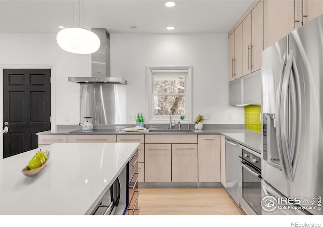 kitchen featuring wall chimney exhaust hood, appliances with stainless steel finishes, light brown cabinetry, light wood-style floors, and a sink