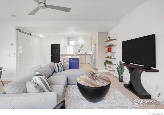 living area with ceiling fan, a barn door, recessed lighting, baseboards, and light wood-type flooring