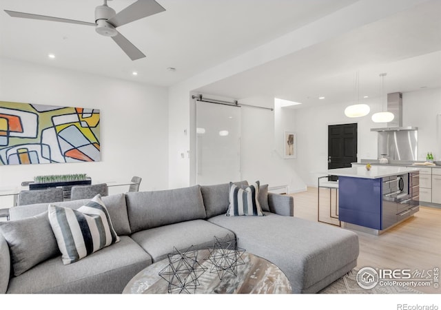 living room featuring a ceiling fan, light wood-type flooring, recessed lighting, and a barn door