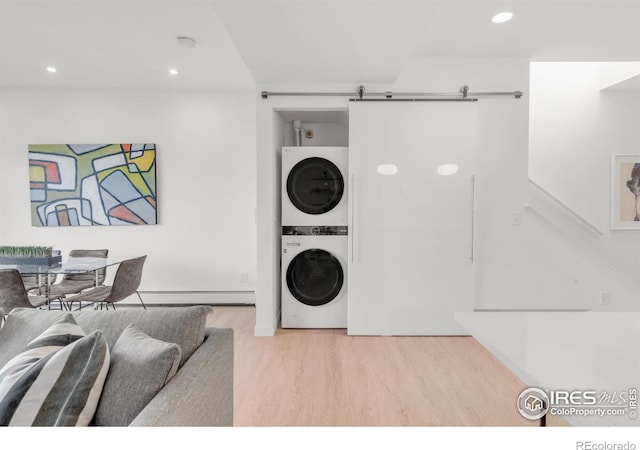 laundry room with a barn door, a baseboard radiator, laundry area, wood finished floors, and stacked washer / drying machine