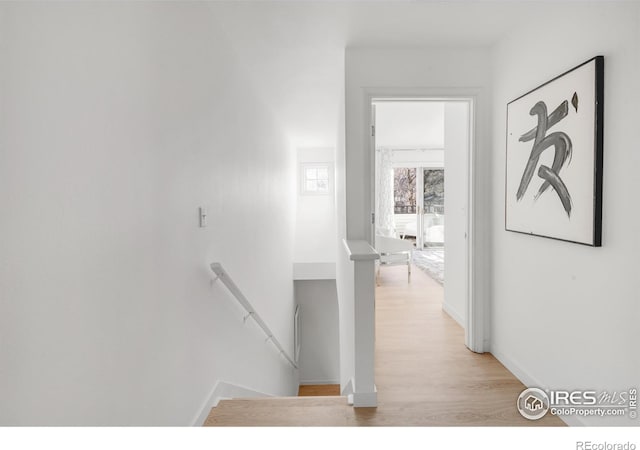 hallway featuring baseboards, an upstairs landing, and light wood-style floors