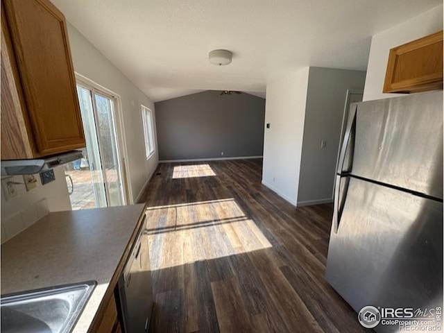 kitchen featuring dark wood-style flooring, brown cabinets, freestanding refrigerator, vaulted ceiling, and baseboards