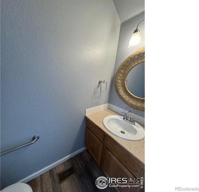 half bathroom featuring visible vents, vanity, baseboards, and wood finished floors