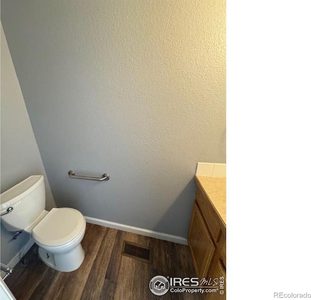 bathroom with toilet, wood finished floors, vanity, visible vents, and baseboards