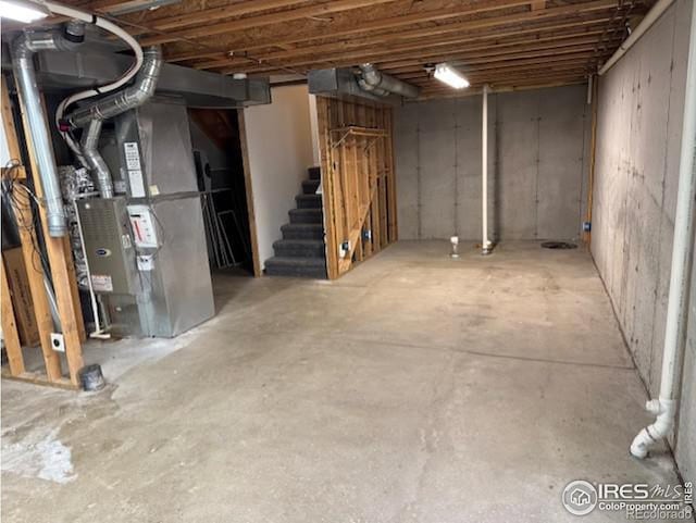 unfinished basement featuring stairway and heating unit