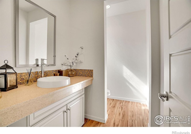 bathroom with backsplash, toilet, vanity, wood finished floors, and baseboards