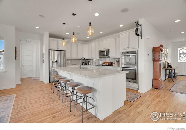 kitchen with stainless steel appliances, a sink, white cabinetry, light wood finished floors, and a kitchen bar