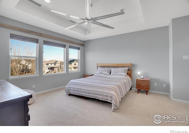 carpeted bedroom featuring ceiling fan, a tray ceiling, visible vents, and baseboards