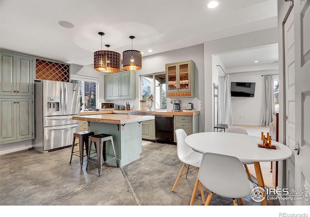 kitchen featuring black dishwasher, butcher block countertops, stainless steel fridge, plenty of natural light, and a kitchen bar