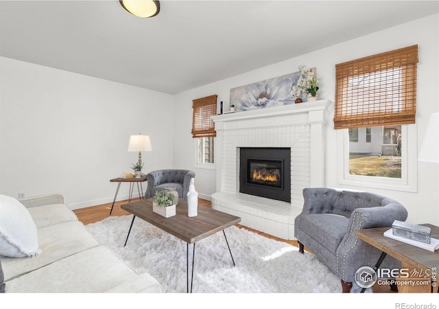 living room with baseboards, a brick fireplace, and wood finished floors