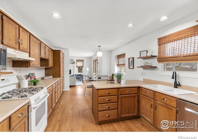 kitchen featuring brown cabinetry, a peninsula, a sink, white gas range oven, and under cabinet range hood