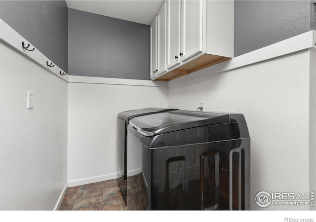 clothes washing area featuring baseboards, cabinet space, stone finish floor, and washer and clothes dryer