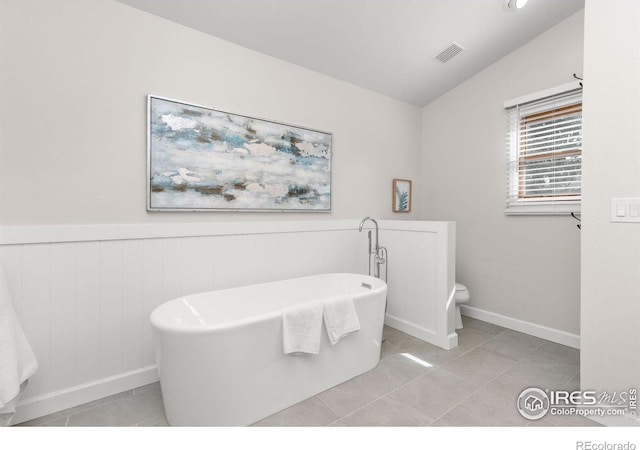 full bath with a wainscoted wall, visible vents, lofted ceiling, a freestanding tub, and tile patterned flooring