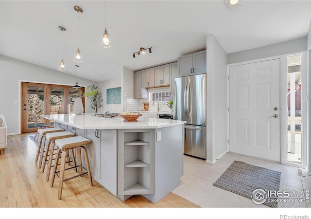 kitchen with light countertops, appliances with stainless steel finishes, gray cabinets, decorative backsplash, and a center island