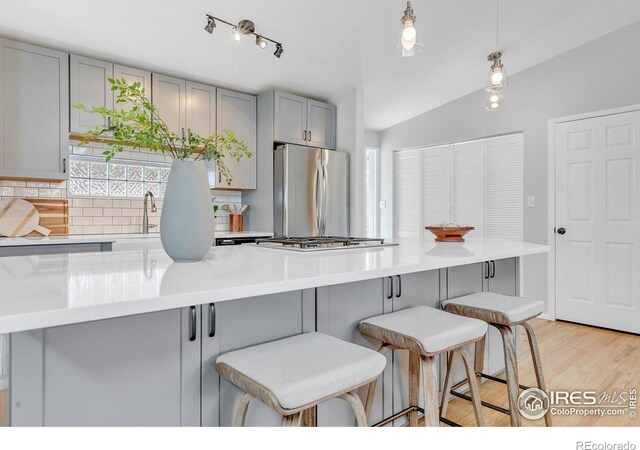 kitchen with stainless steel appliances, decorative backsplash, gray cabinetry, vaulted ceiling, and a kitchen breakfast bar