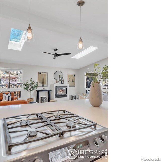 kitchen featuring a ceiling fan, stovetop, lofted ceiling with skylight, a glass covered fireplace, and decorative light fixtures