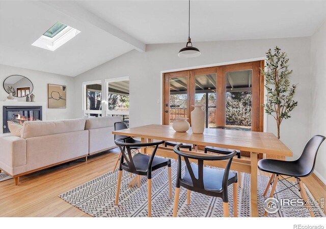 dining space with lofted ceiling with skylight, light wood-style flooring, and a glass covered fireplace