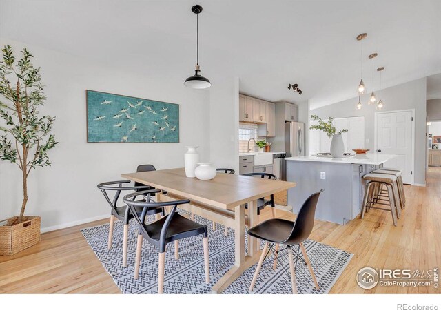 dining space with baseboards, vaulted ceiling, and light wood finished floors