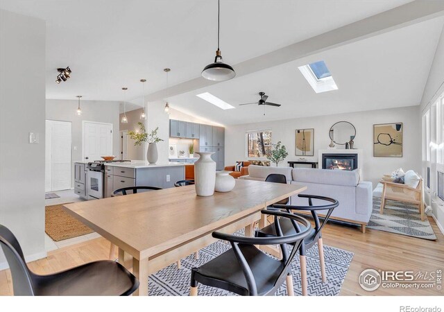 dining space featuring lofted ceiling with skylight, a ceiling fan, and light wood-style floors