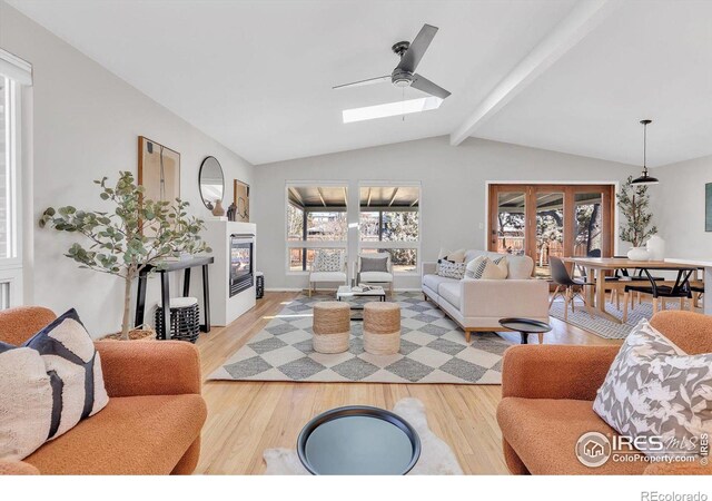 living area with vaulted ceiling with skylight, light wood finished floors, a glass covered fireplace, and french doors