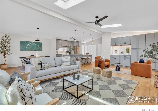 living area with light wood-type flooring, vaulted ceiling with skylight, and a ceiling fan