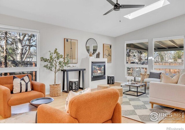 living area with vaulted ceiling with skylight, light wood finished floors, plenty of natural light, and a glass covered fireplace