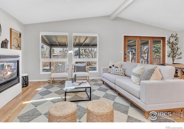 living room featuring vaulted ceiling with beams, wood finished floors, a glass covered fireplace, and baseboards