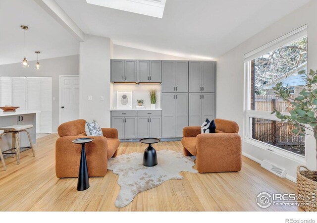 living room featuring lofted ceiling with skylight, light wood-type flooring, visible vents, and baseboards