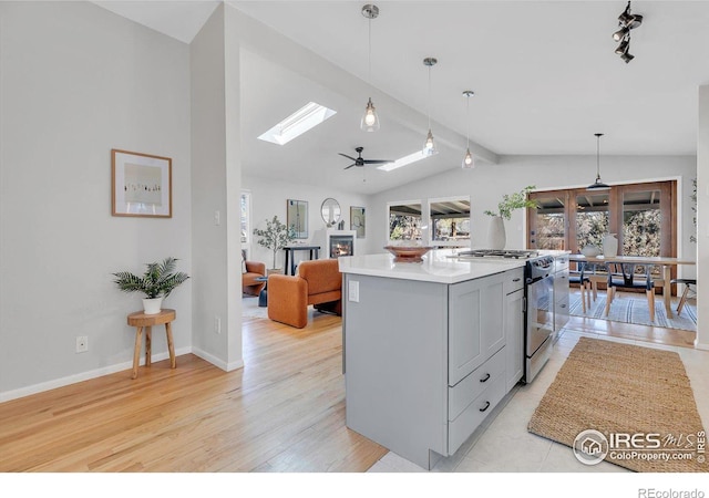 kitchen with vaulted ceiling with skylight, a center island, light countertops, gray cabinets, and stainless steel range with gas stovetop